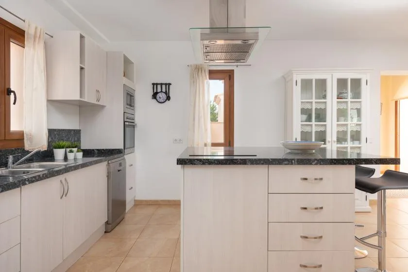 Una cocina luminosa con gabinetes blancos, encimeras oscuras y una isla central.