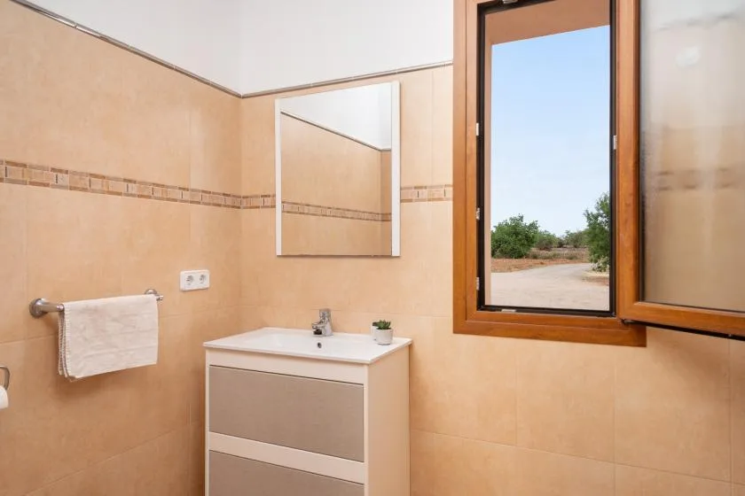 Un baño alicatado con lavabo, espejo de pared y una ventana abierta.
