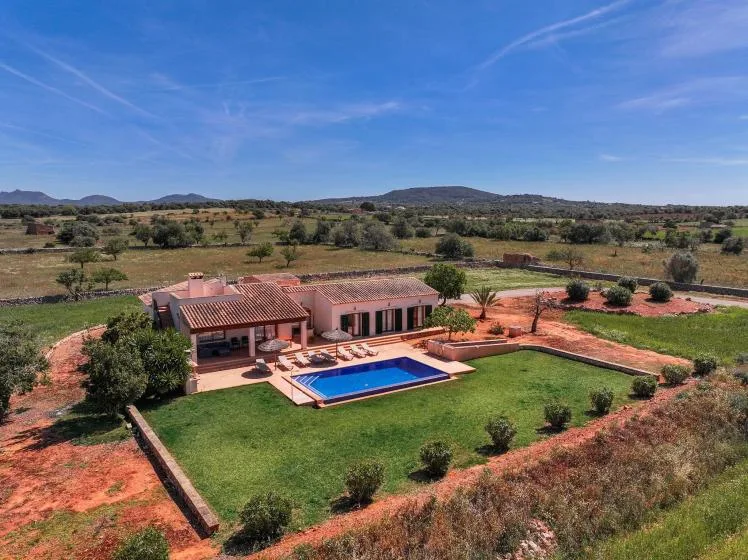 Una casa y una piscina están en un jardín cuidado en campo abierto.