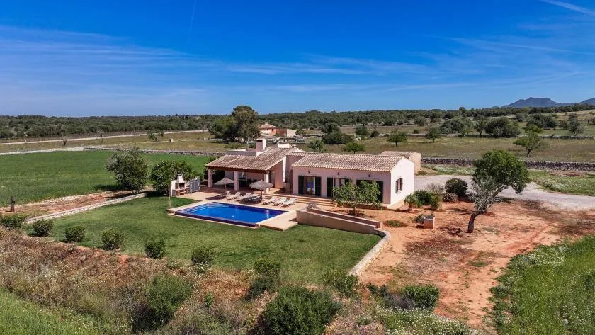Una casa de campo junto a una piscina, rodeada de campos verdes y terreno abierto.