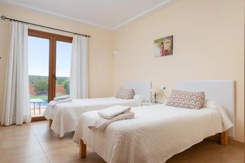 Un dormitorio con dos camas vestidas con ropa de cama clara junto a una ventana alta.