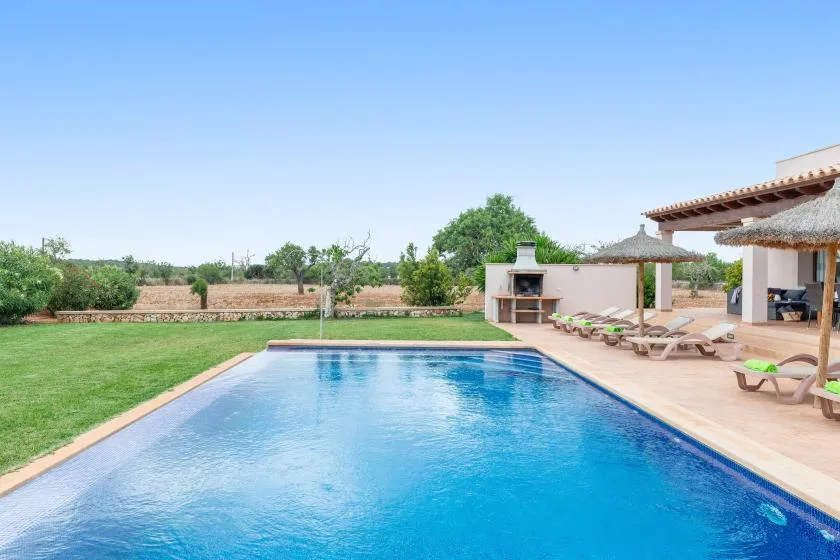 Una piscina junto a un césped y una zona de estar al aire libre.