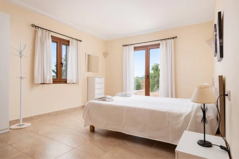 Un dormitorio luminoso con una cama bien tendida y dos ventanas con cortinas.