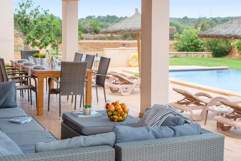 Un patio cubierto con asientos al aire libre y una mesa de comedor junto a una piscina.