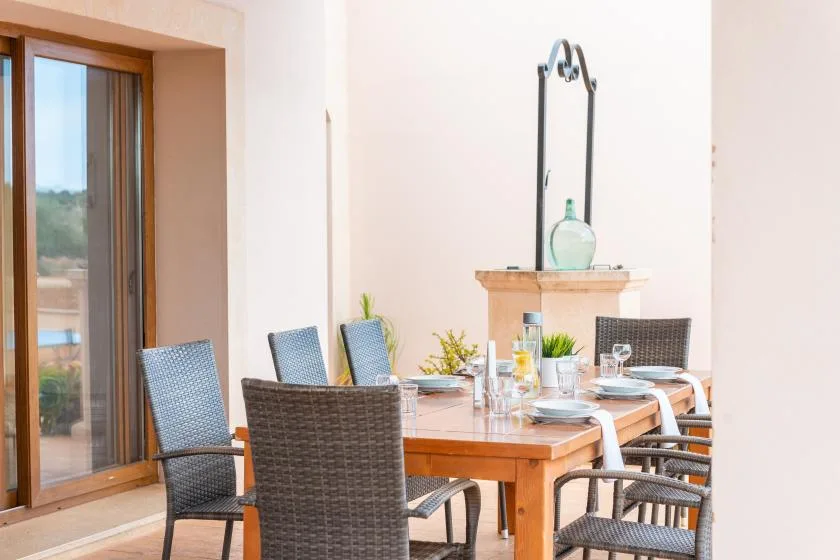 Una zona de comedor al aire libre con una mesa de madera y asientos tejidos junto a una puerta corrediza de vidrio.