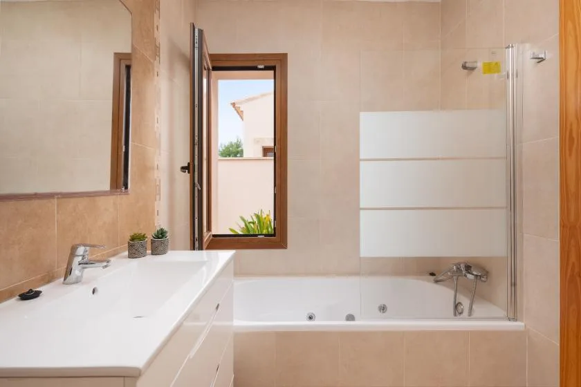 Un baño revestido de azulejos con bañera, grifería de ducha y un largo lavabo.