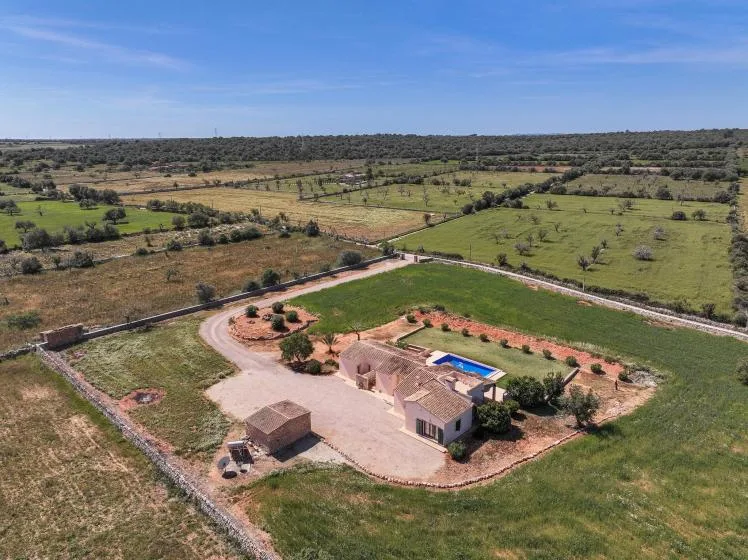 Vista aérea de una propiedad rural rodeada de campos, con un edificio pequeño y una piscina.