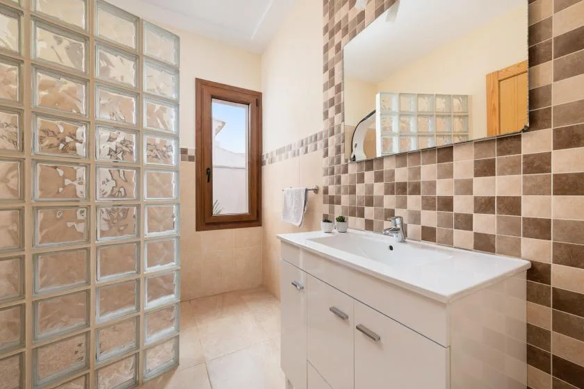 Un baño con lavabo, espejo de pared y tabique de bloques de vidrio.