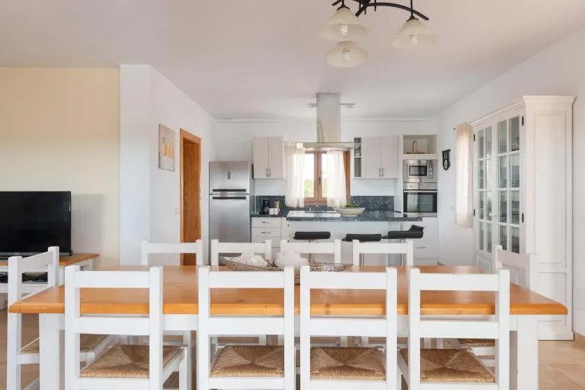 Comedor y cocina de concepto abierto con una mesa larga y muebles blancos.