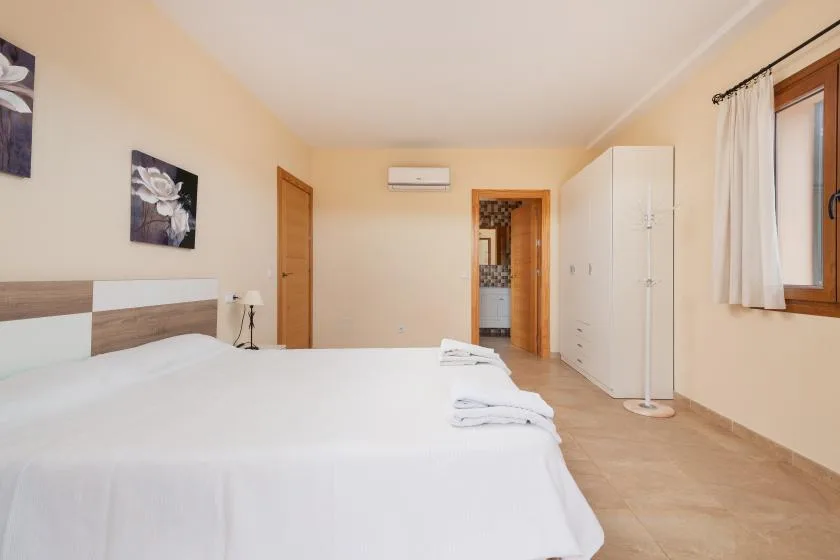 Un dormitorio con una cama bien tendida y un armario junto a la ventana.