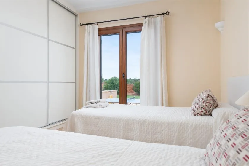 Un dormitorio luminoso con dos camas y una ventana enmarcada por cortinas blancas.
