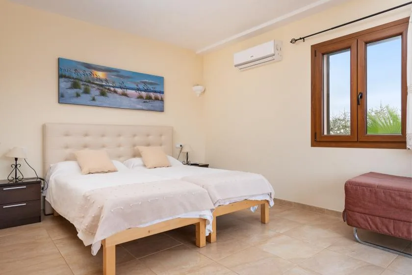 Un dormitorio luminoso con dos camas, una mesita de noche y una ventana.