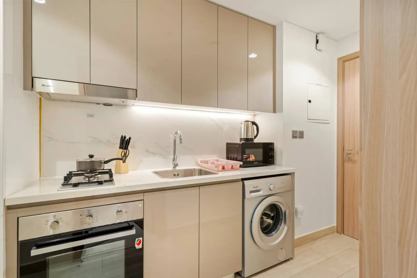 Una cocina compacta con gabinetes claros, una placa de cocción y una lavadora.