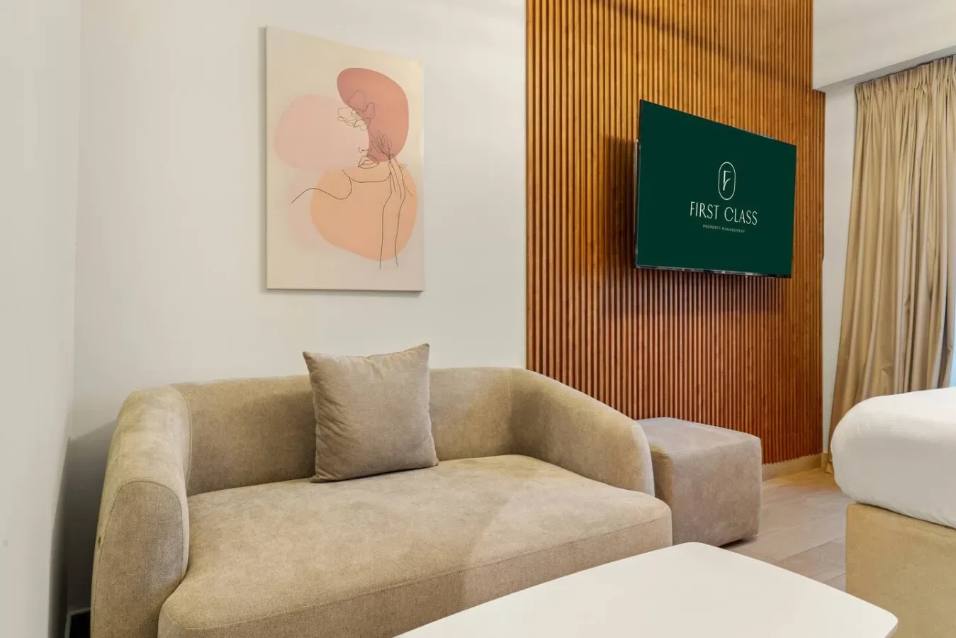 A bedroom seating area with a beige sofa beside a bed and wall-mounted television.
