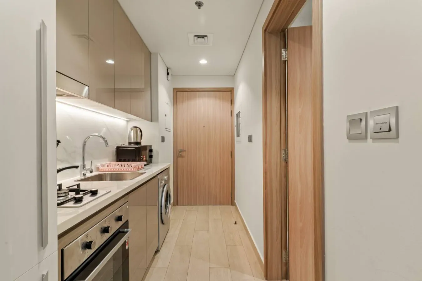 Un pasillo estrecho con cocina, armarios y una puerta de madera al fondo.