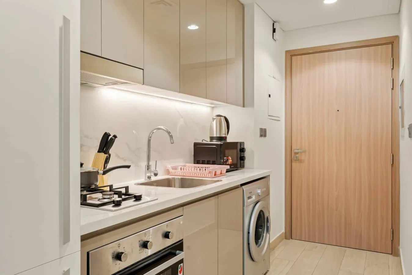 Una cocina compacta con encimera, fregadero y electrodomésticos junto a una puerta de madera.
