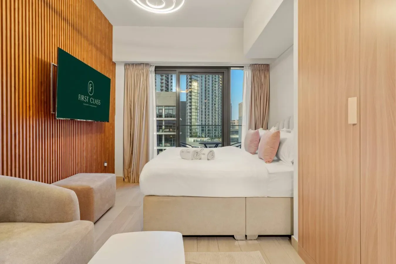 A bedroom with a bed, seating, and a large window overlooking nearby buildings.