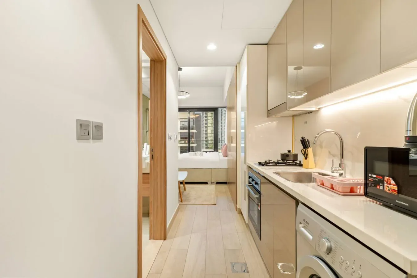 Una cocina estrecha con gabinetes claros y una encimera conduce a un baño.