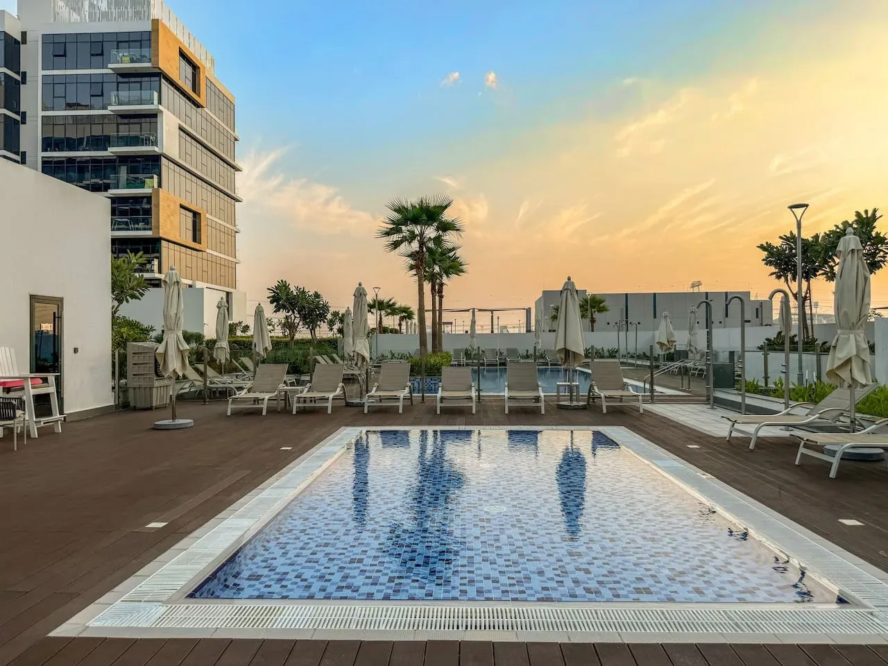 Una terraza con piscina y asientos para descansar junto a un edificio moderno al atardecer.