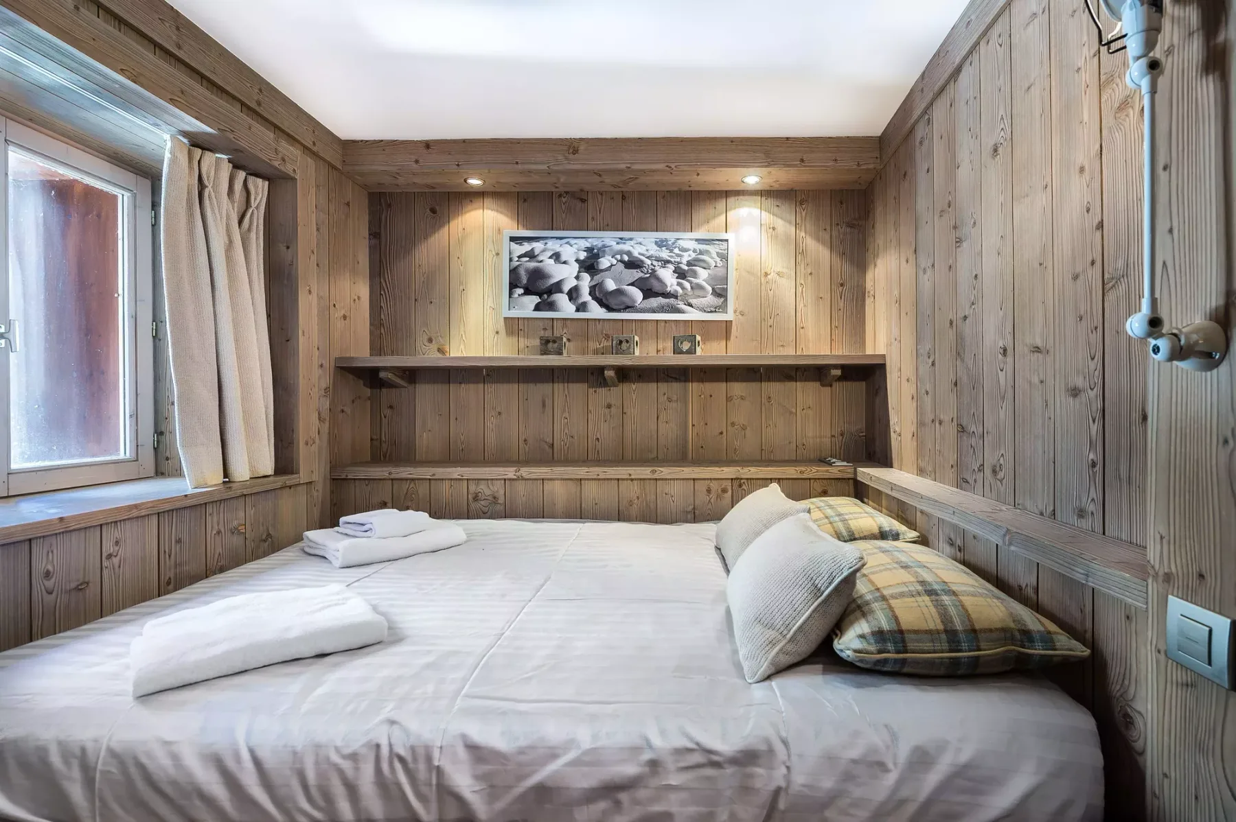 Una cama ocupa una habitación revestida de madera, con toallas dobladas y almohadas encima.