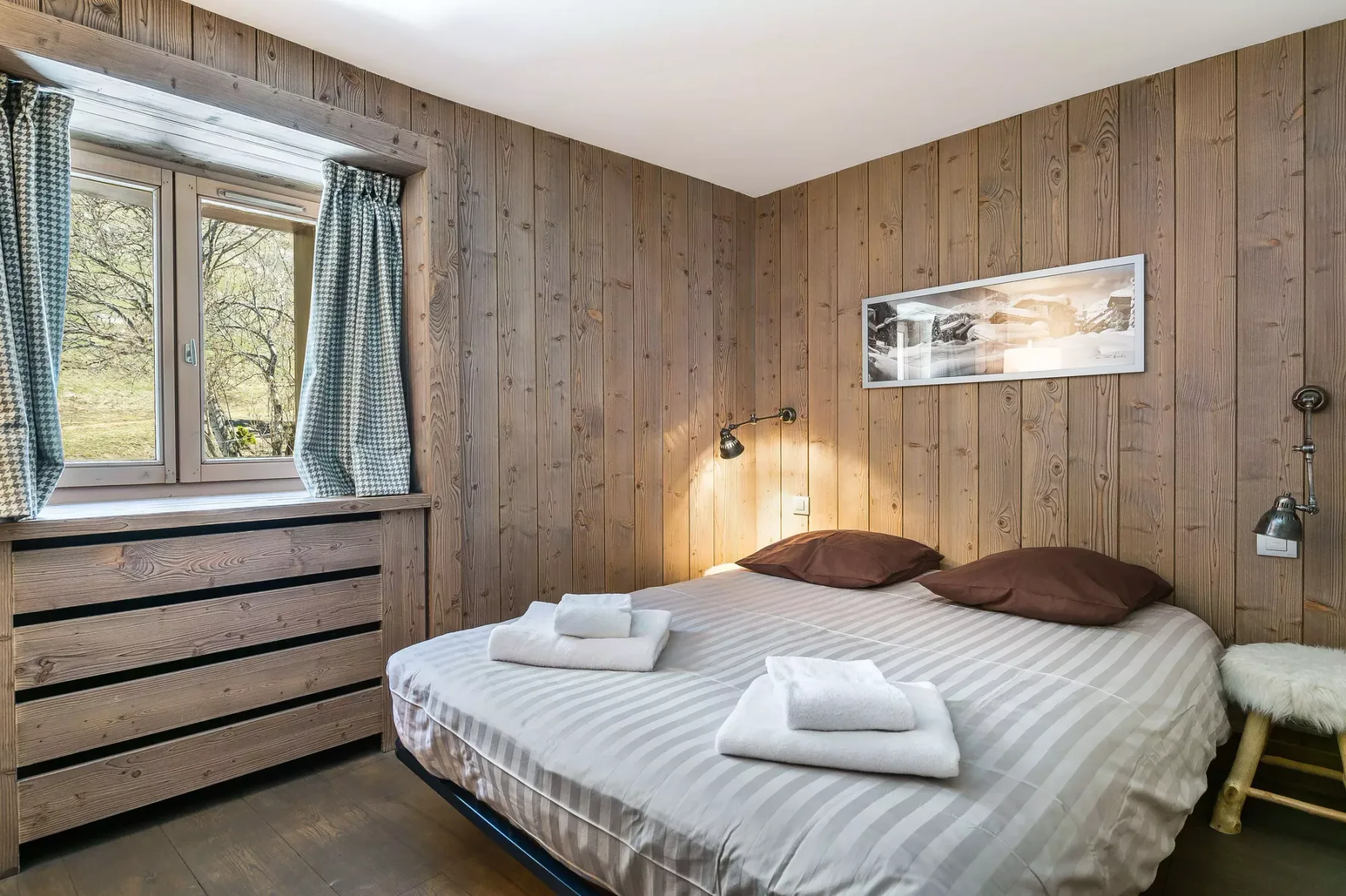 Un dormitorio con una cama, toallas dobladas y una ventana con vistas a los árboles.
