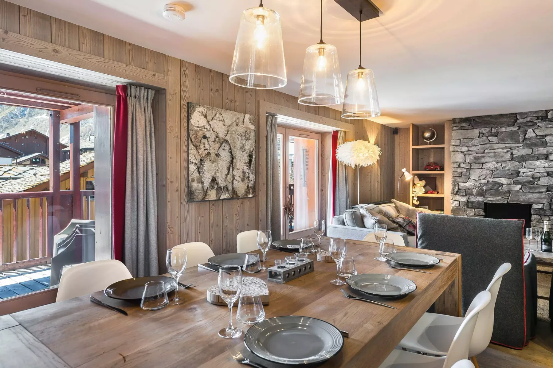 A dining area with a long wooden table set beside large windows.