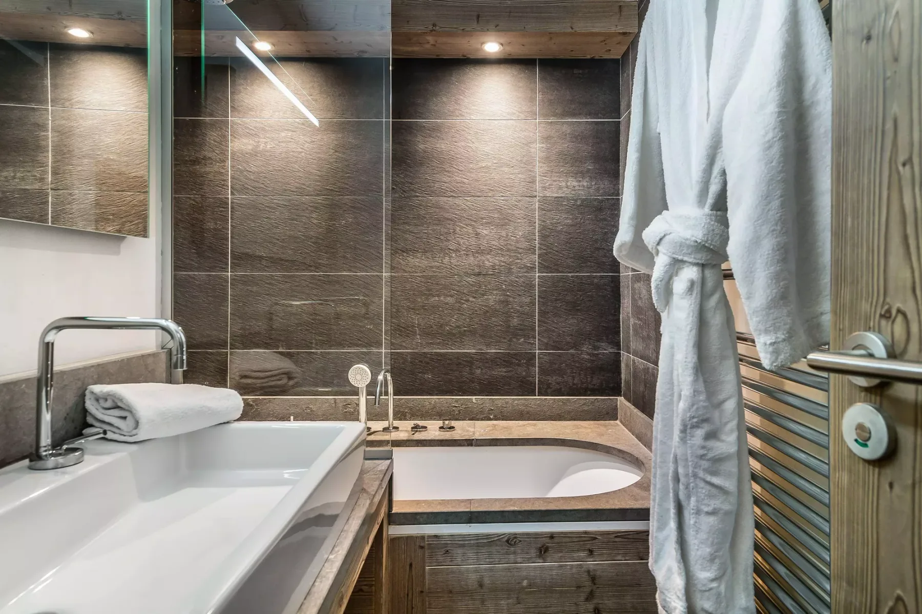 Un baño alicatado con bañera, lavabo y batas colgadas.