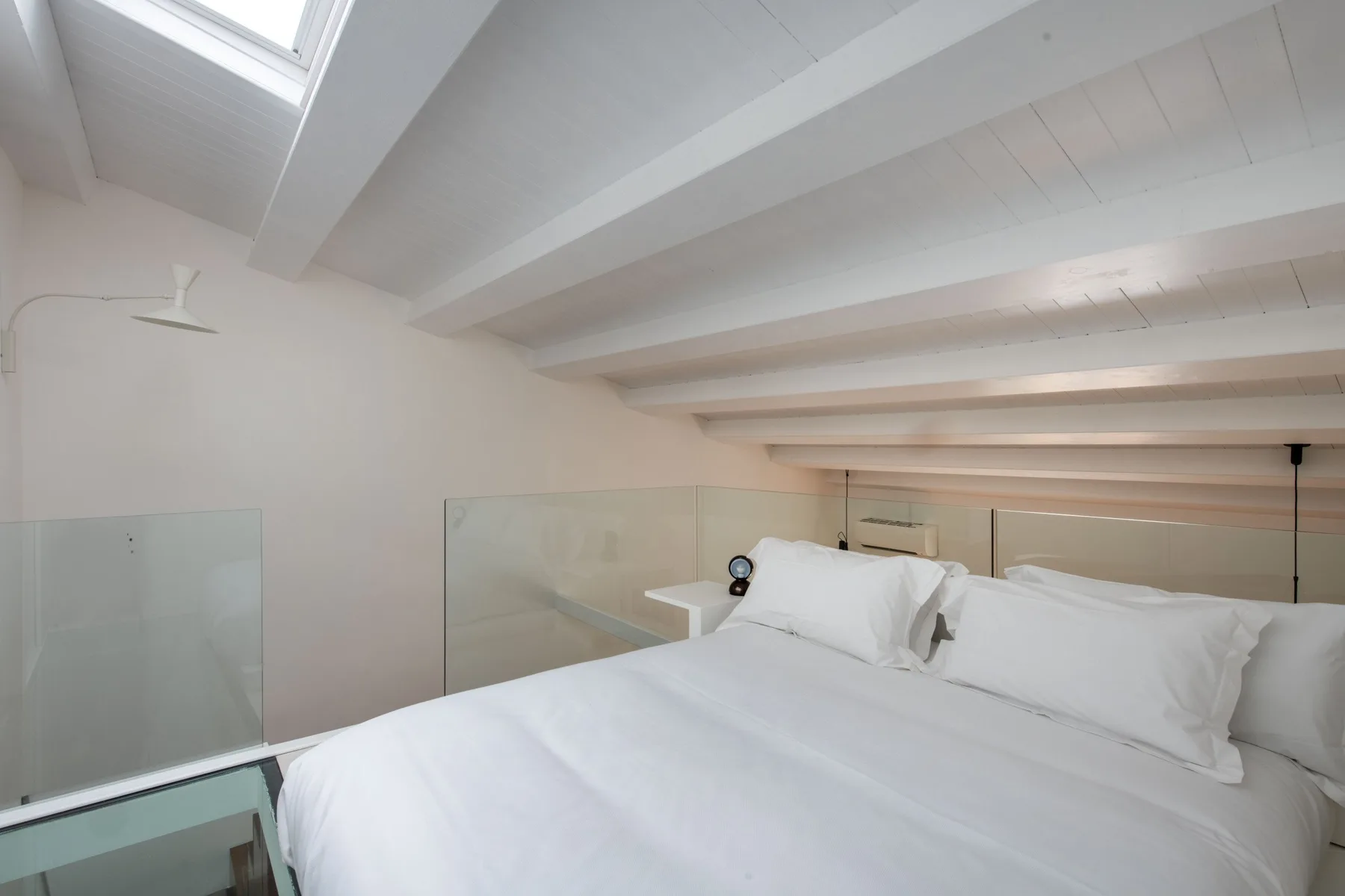 A bright bedroom with a large bed beneath a sloped ceiling and skylight.