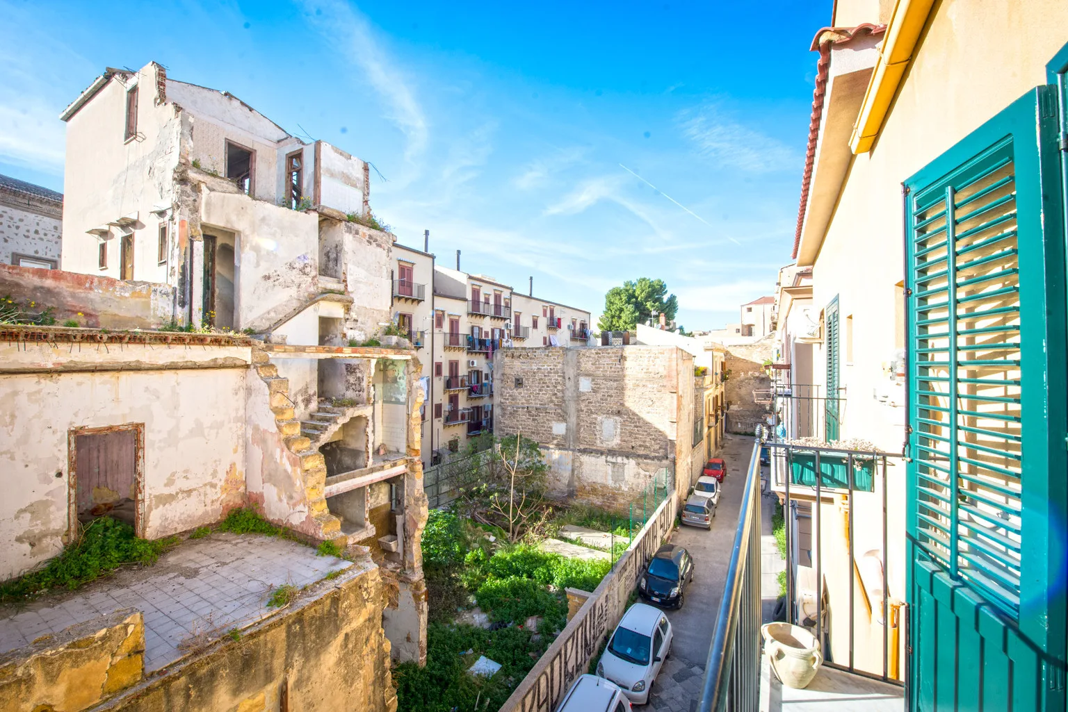 A balcony overlooks a narrow street and weathered buildings under a clear blue sky.