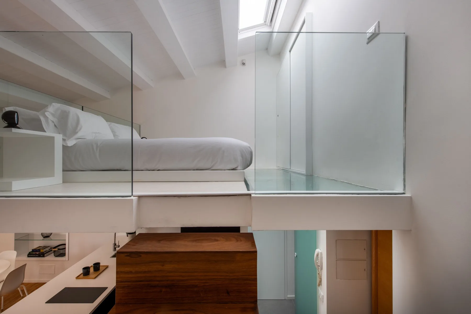 A loft bedroom with a raised bed beside a glass partition.