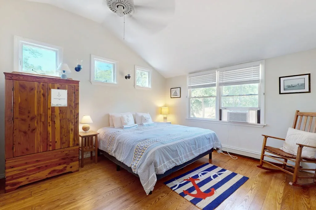A bright bedroom with a bed, wooden flooring, and windows along the wall.
