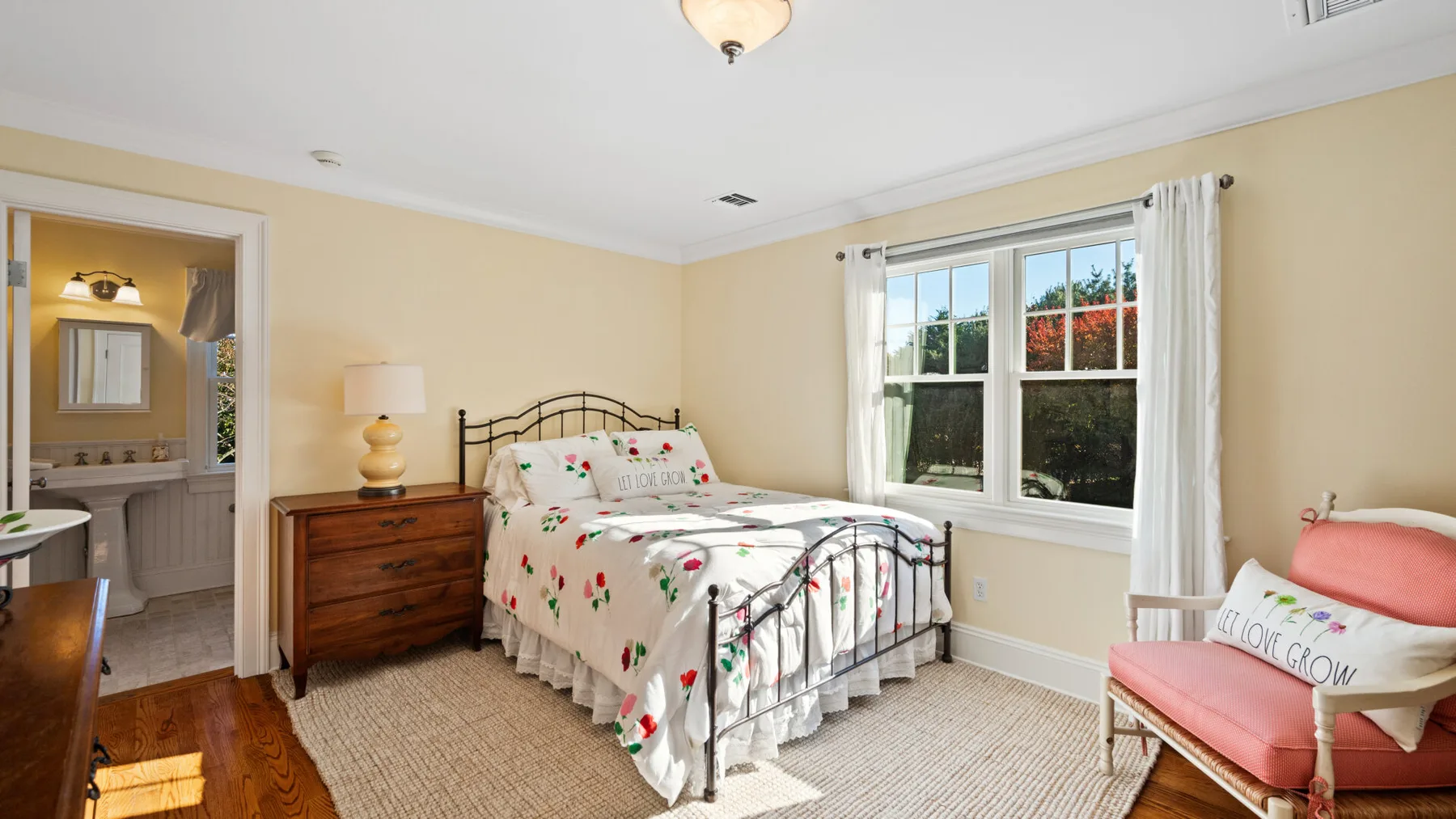 Un dormitorio con una colcha floral, una cómoda de madera y una ventana.