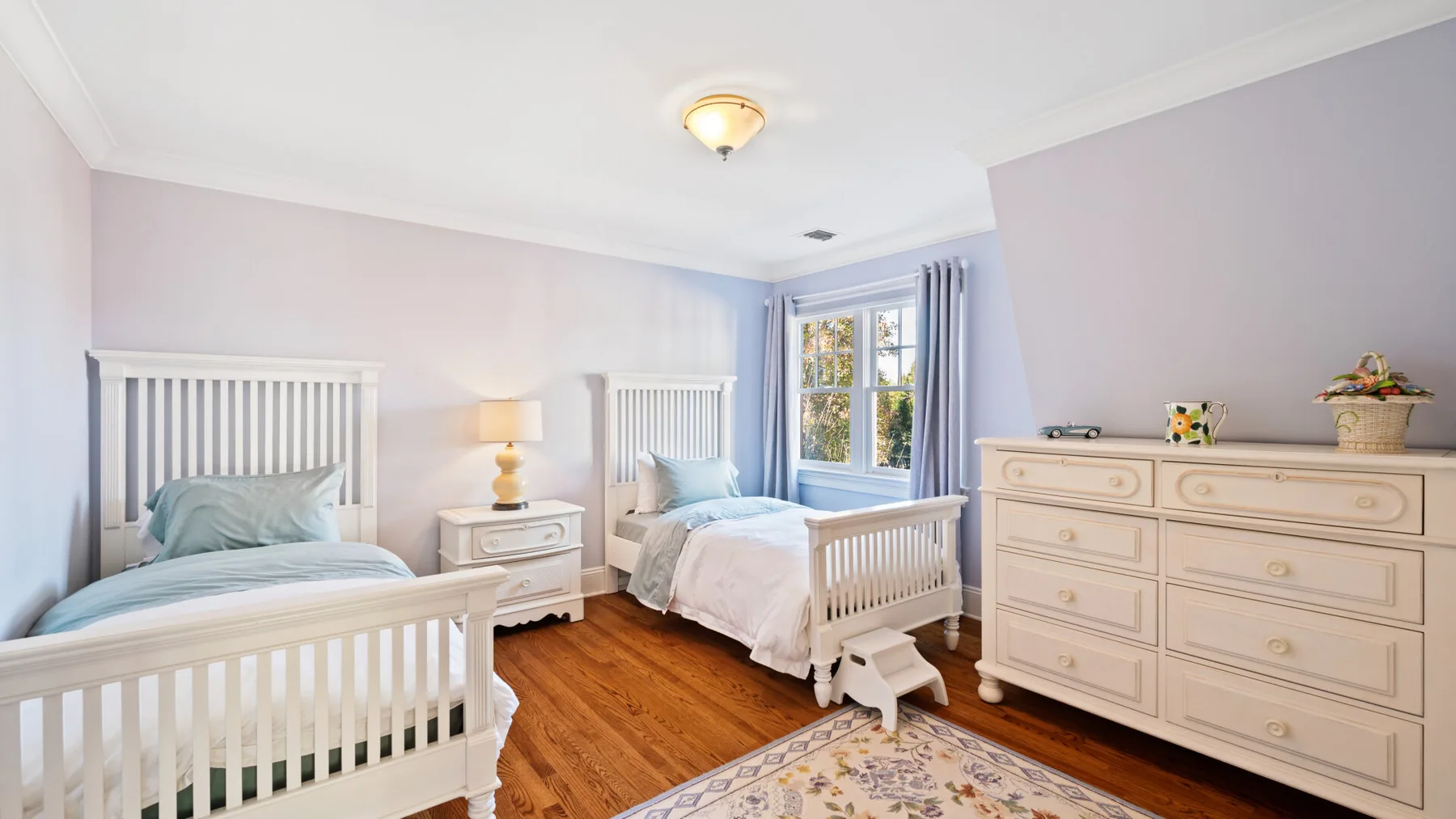 Un dormitorio luminoso con dos camas, una ventana y una cómoda.