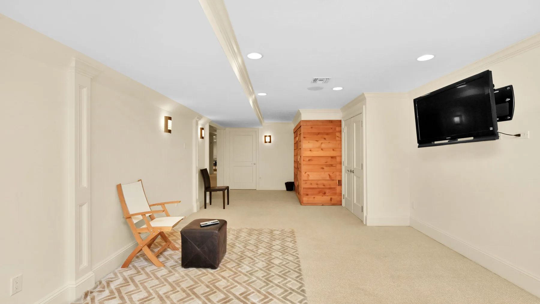 Una habitación de sótano terminada con una alfombra estampada, sillas plegables y un televisor montado en la pared.