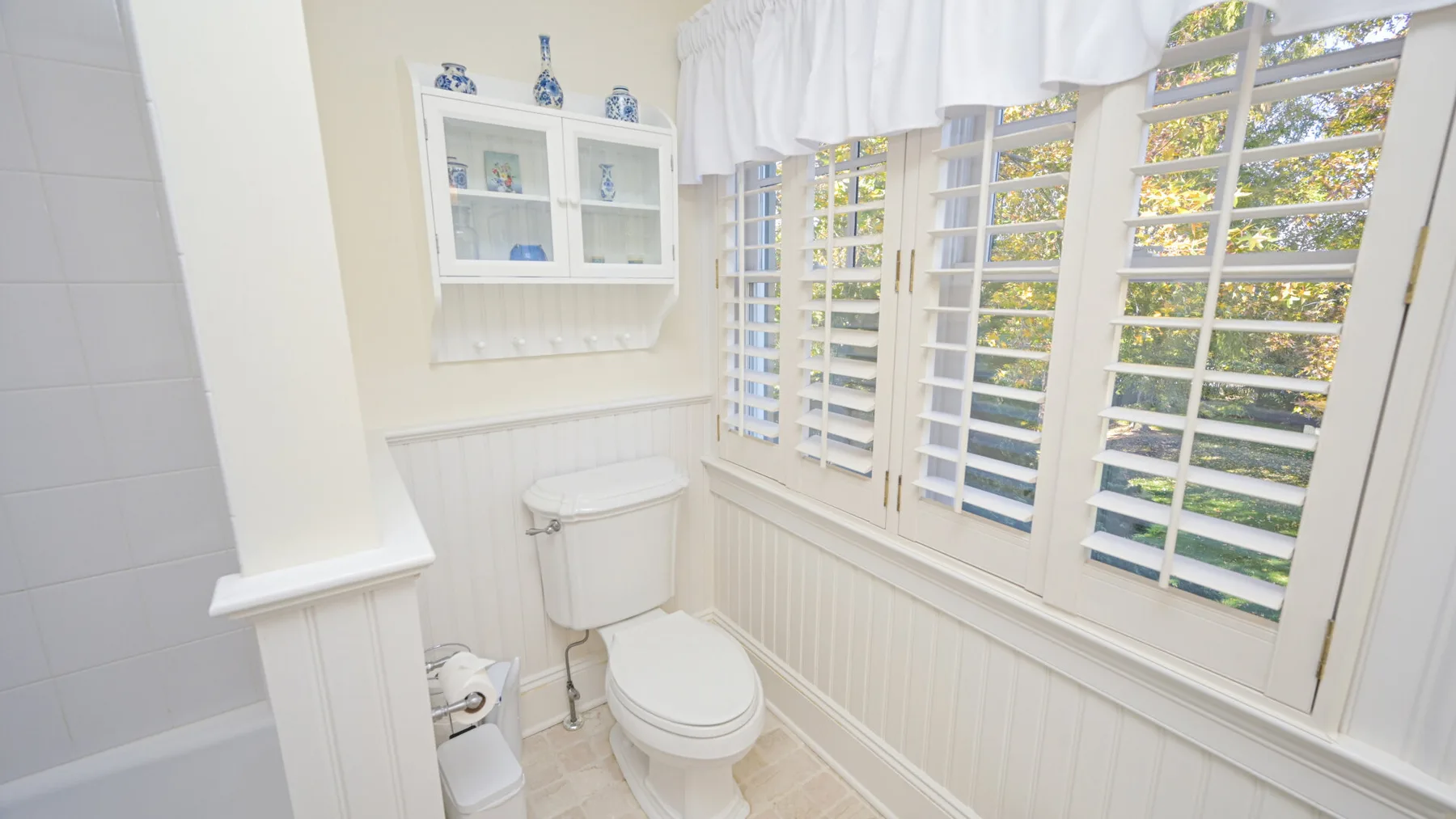 Un baño luminoso con inodoro, lavabo y ventanas con contraventanas.