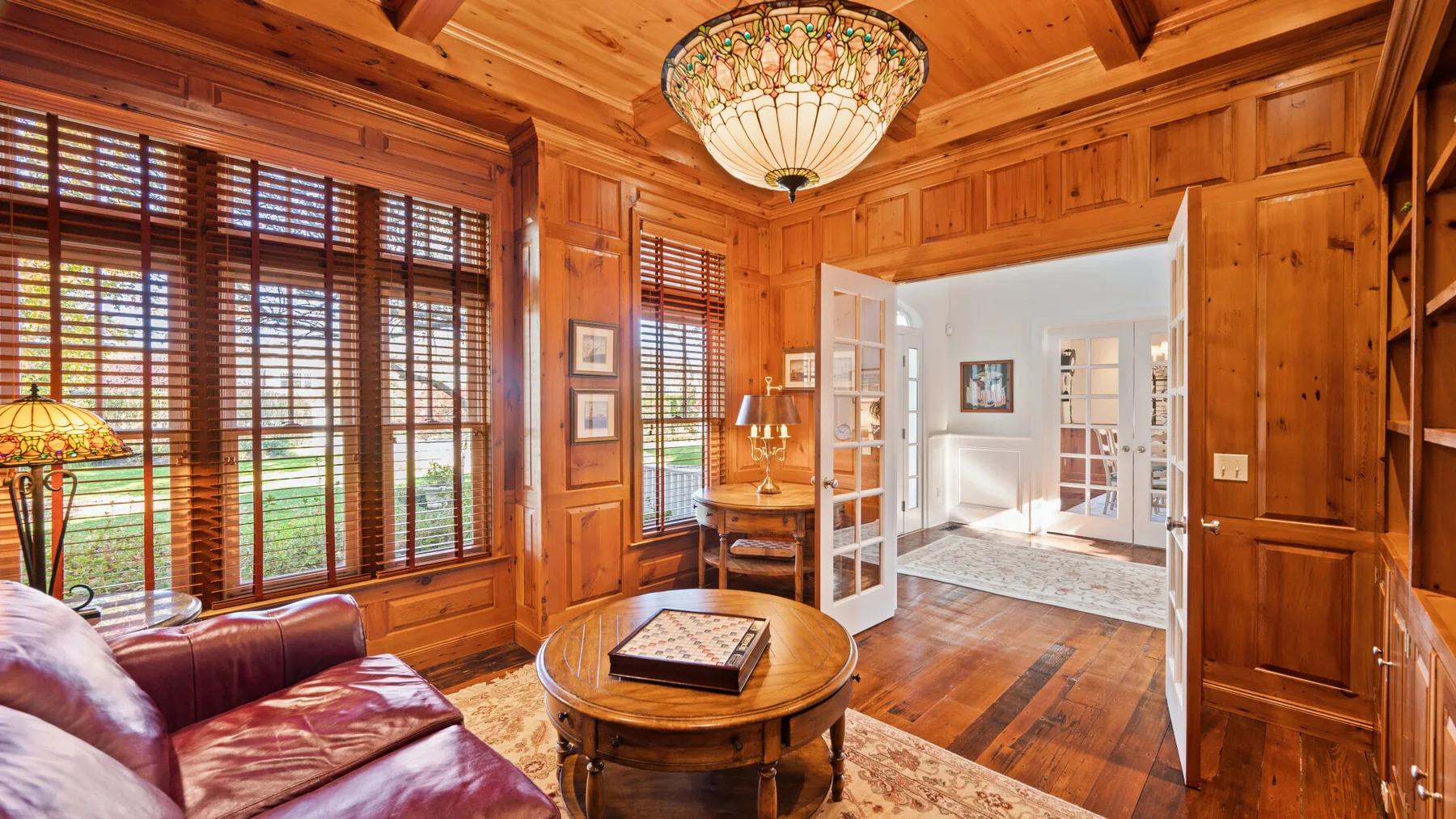 Una sala con paneles de madera se abre mediante puertas dobles a una habitación luminosa.