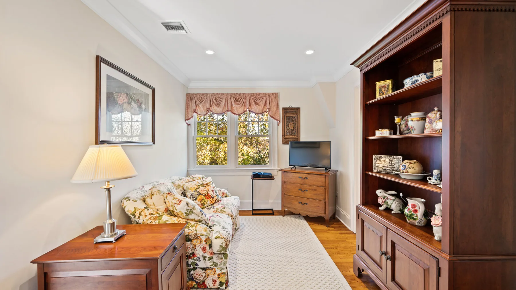 Una luminosa sala de estar con asientos florales, un mueble de madera y una gran estantería.