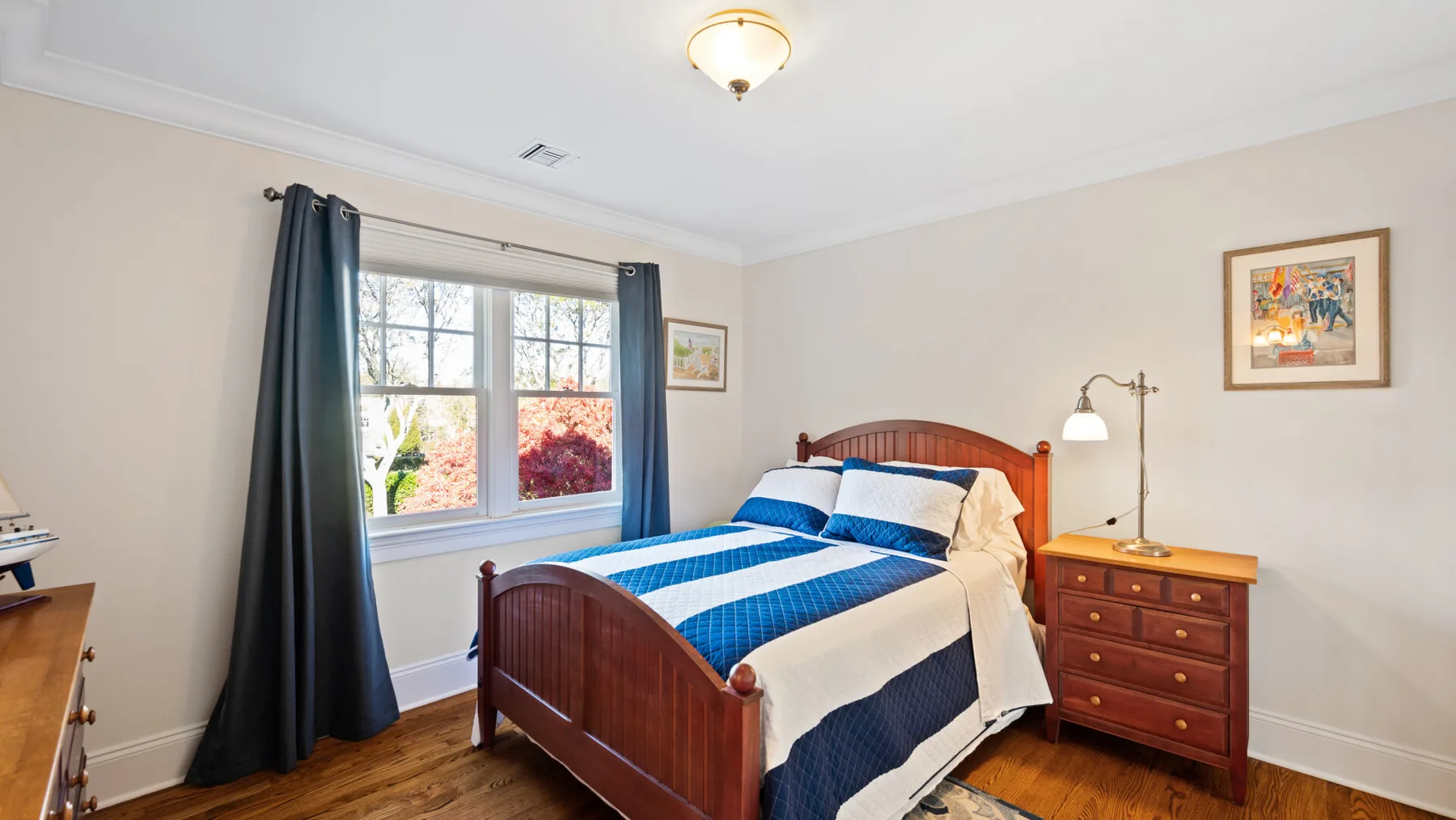 Un dormitorio con una cama de madera vestida con ropa de cama azul y blanca junto a una ventana.