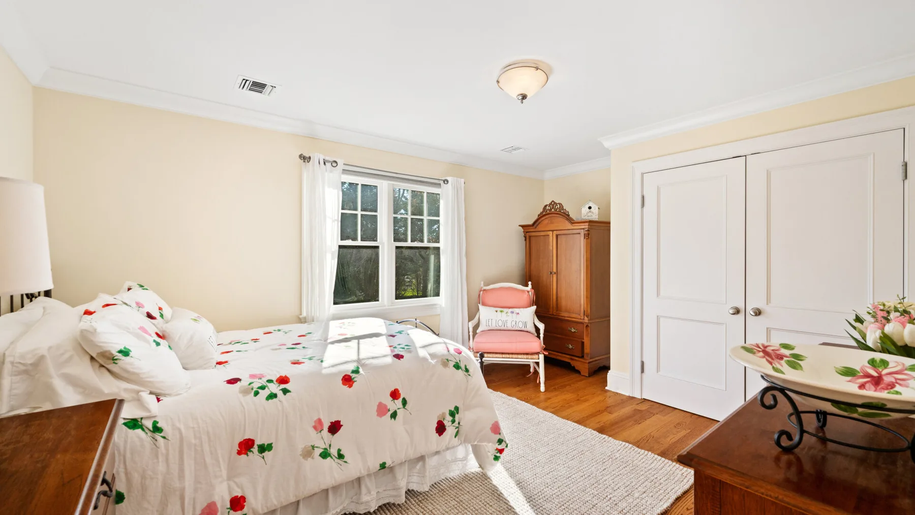Un dormitorio con una colcha floral, una ventana y un armario de madera.