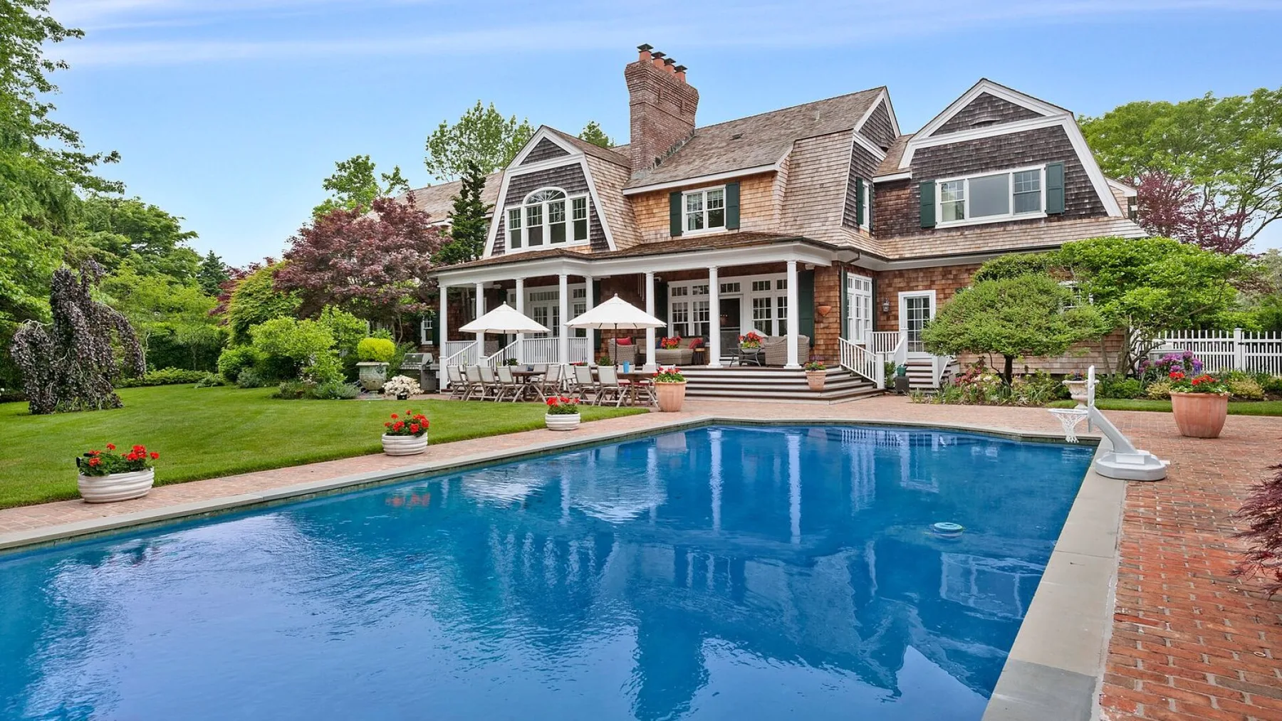 Una casa grande da a una piscina, con césped verde y jardín.