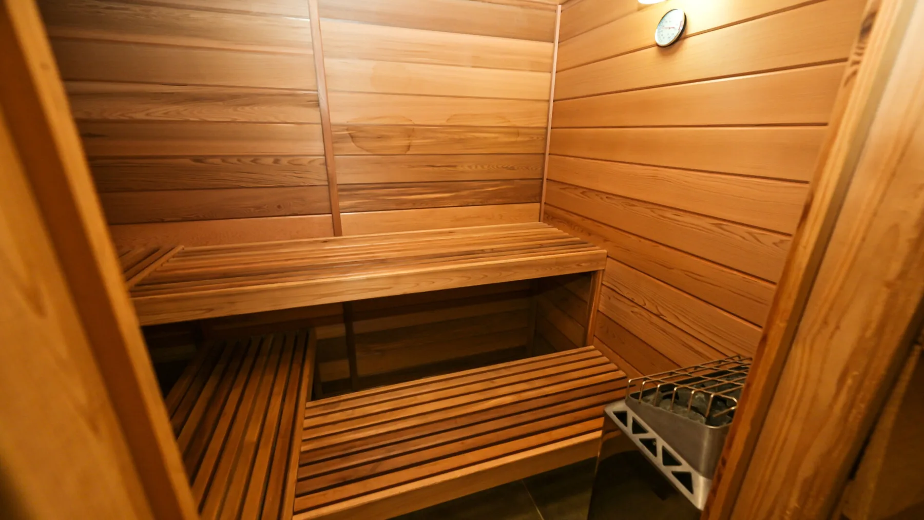 Una sauna de madera con asientos escalonados y un pequeño indicador redondo en la pared.