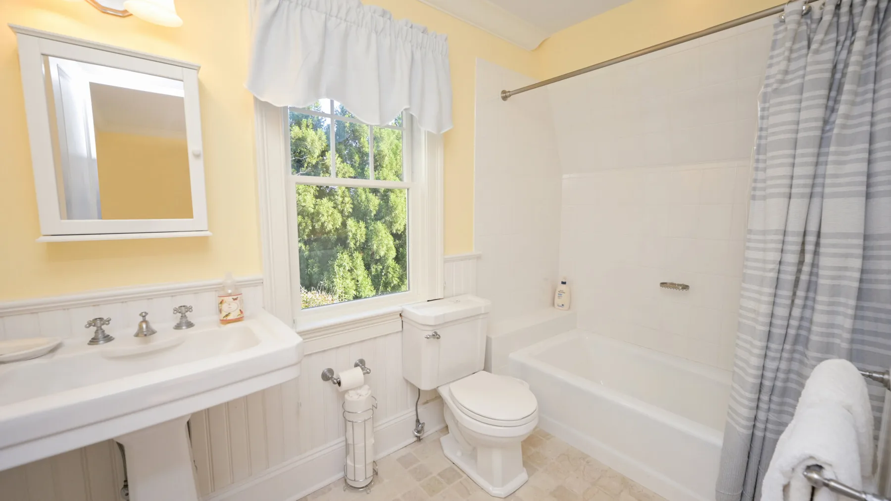 Un baño con lavabo, inodoro y bañera junto a una ventana con cortina.