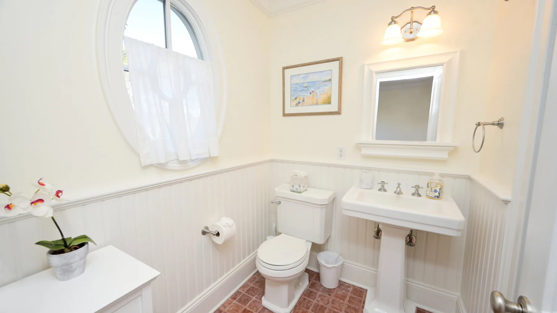 Un baño luminoso con lavabo, inodoro y una ventana arqueada.