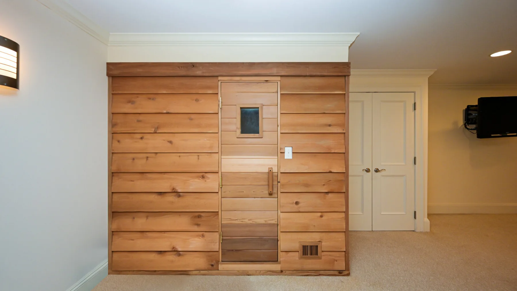 Una habitación con paneles de madera, una puerta de madera en el centro y un televisor en la pared.