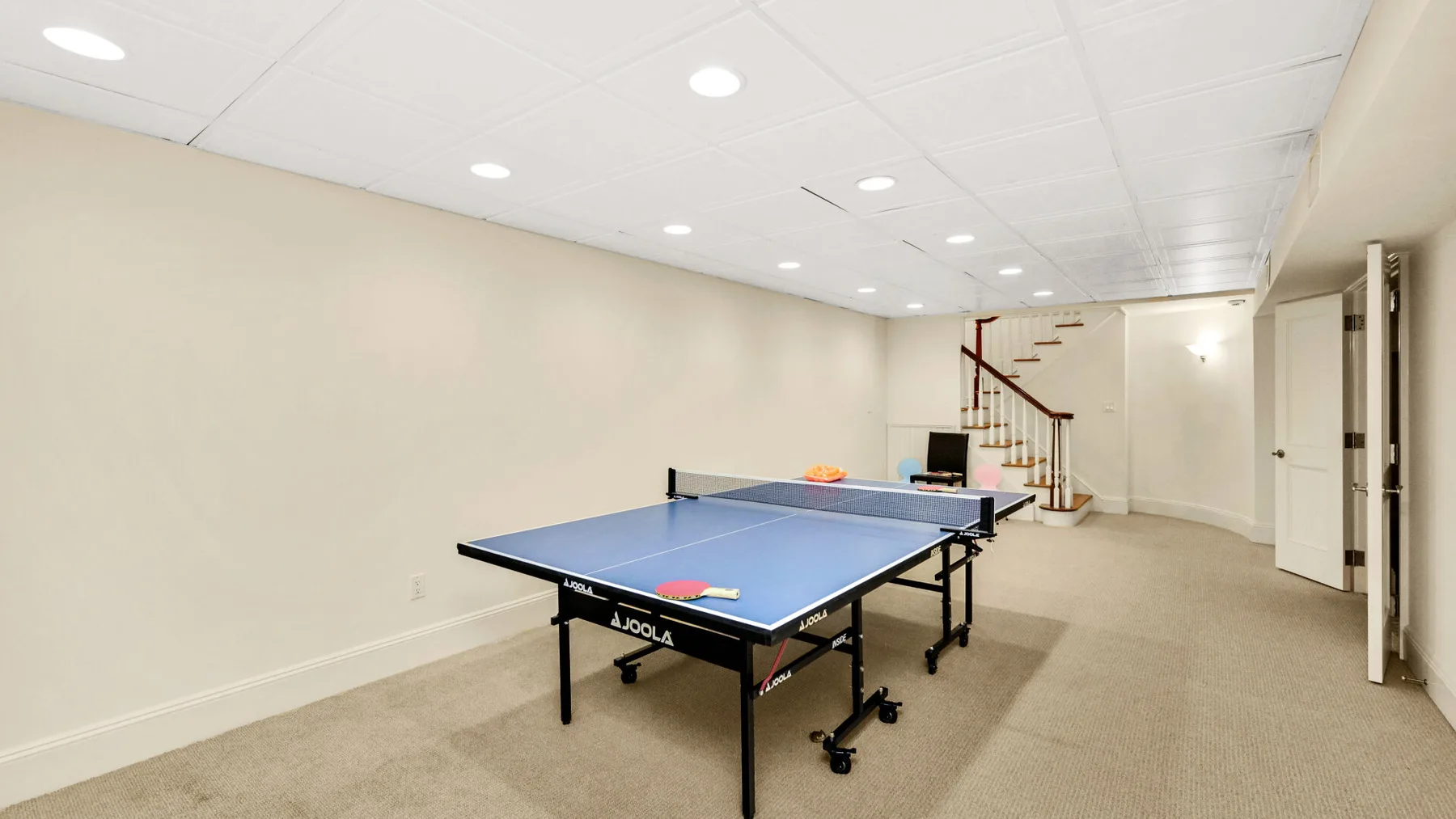 Una sala de recreación en el sótano con una mesa de ping-pong azul y una escalera.