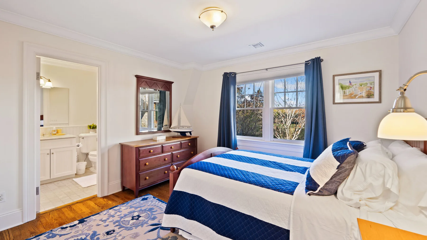 Un dormitorio luminoso con una cama azul y blanca junto a una ventana con cortinas azules.