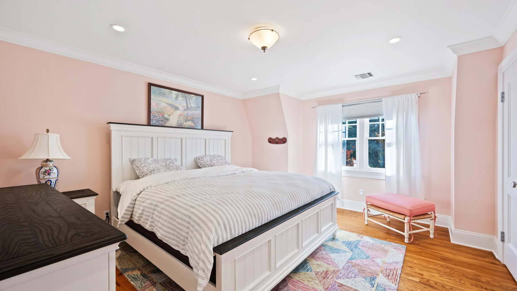 Un dormitorio con una cama grande, paredes rosas y una ventana con cortinas blancas.