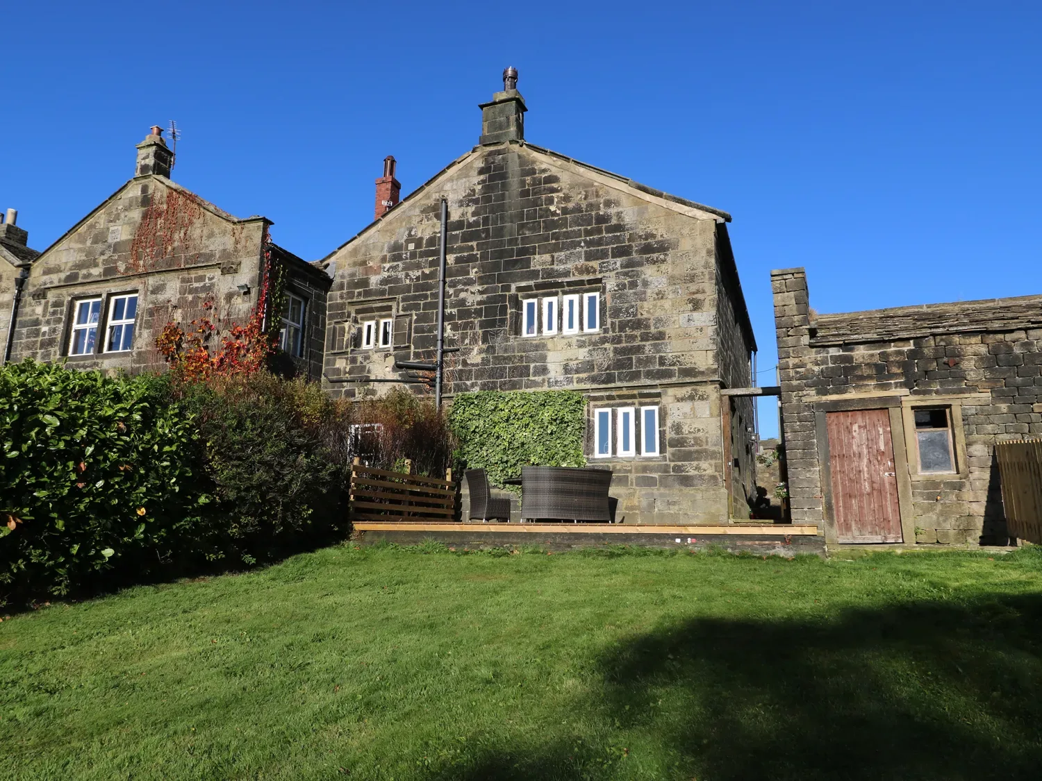 An outdoor view of a stone house with small windows and a lawn with outdoor furniture at The Cottage Beeston Hall in Ripponden