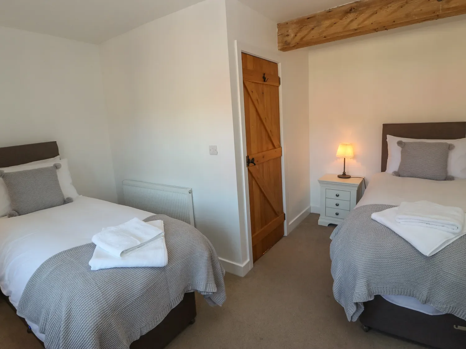 A bedroom with two single beds a wooden door a nightstand with a lamp and folded towels at The Cottage Beeston Hall in Ripponden