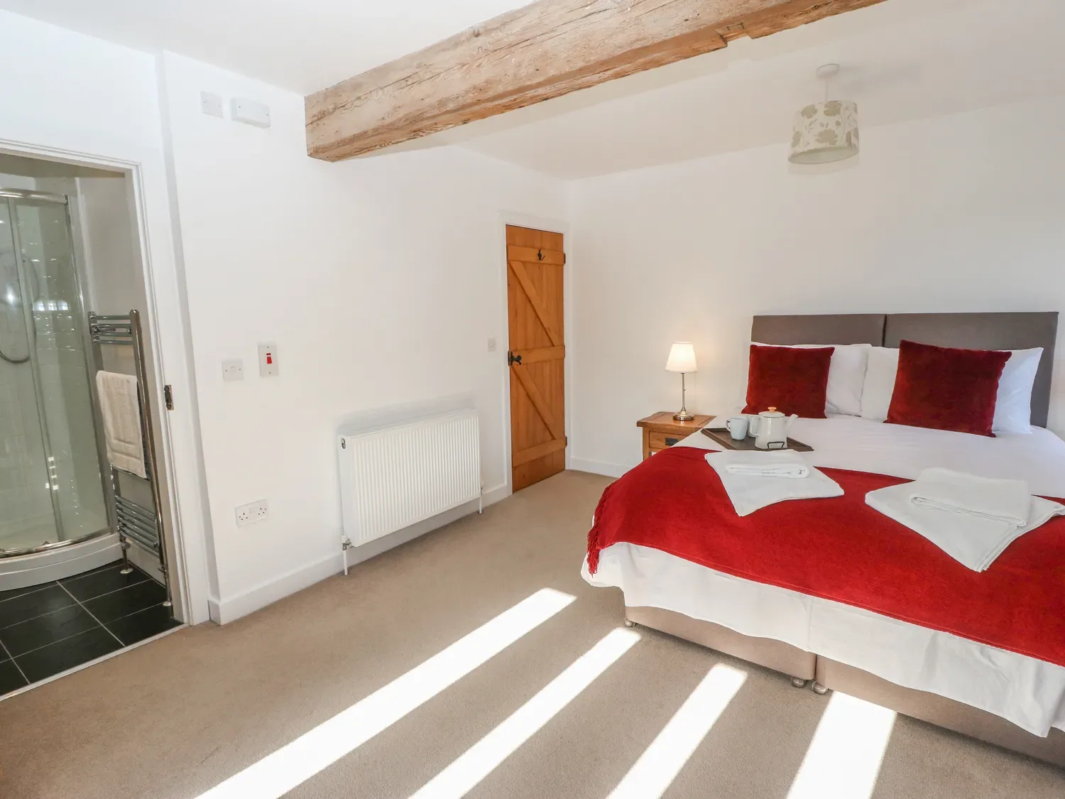 A bedroom with a bed covered in red bedding beside an open bathroom.